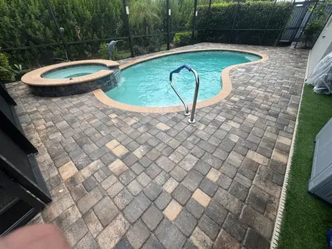 Backyard pool and stone paver deck inside a screened enclosure