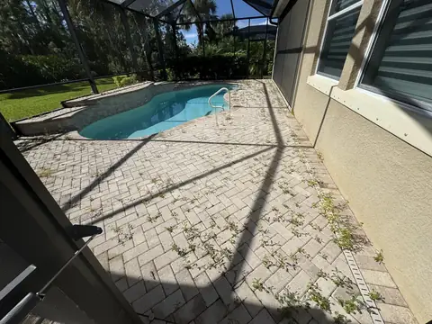 Brick paver pool deck with weeds growing between the pavers inside a screen enclosure